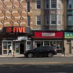 Image of a street iwth four lanes for traffic, three parked cars, and a series of shops, such as center city deli, hi five, Ocean Therapy, and casino city barber and salon