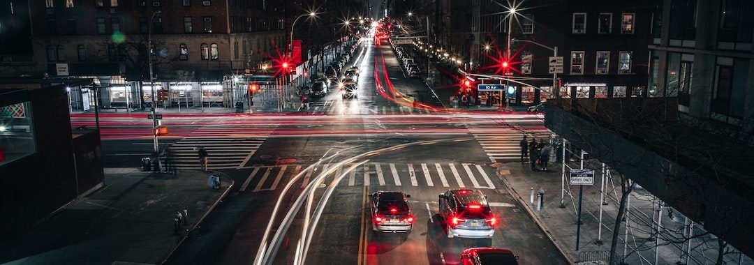 Image of an intersection at night, a long exposure has made the cars driving by appear as lines of light