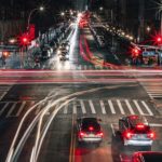 Image of an intersection at night, a long exposure has made the cars driving by appear as lines of light