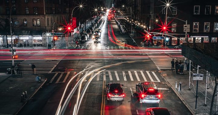 Image of an intersection at night, a long exposure has made the cars driving by appear as lines of light